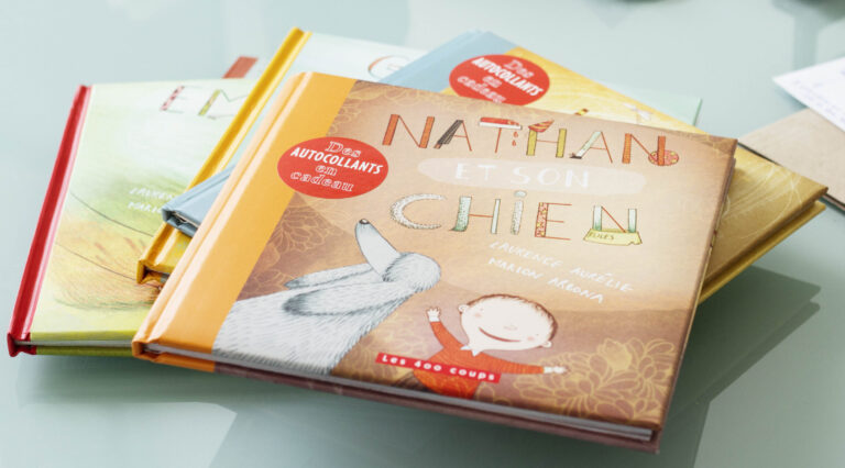 Pile de livres pour enfants dont on voit en partie les couvertures, disposée sur une table. Le premier livre sur la pile est Nathan et son chien.